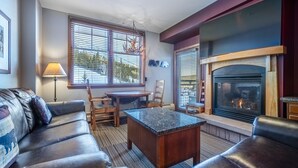 A living room with a fireplace, leather sofa, and a dining table with chairs. - Ski in/Ski out condo w/great views. Overlooking the slopes. Access to hot tub (Winter Park)