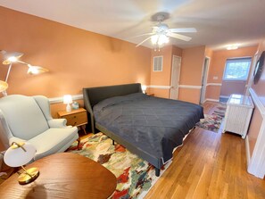 A bedroom with a bed, a chair, a nightstand, a lamp, a ceiling fan, and a window.