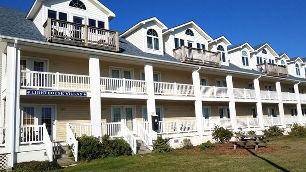 A row of white, multi-story buildings with balconies and a sign reading "Lighthouse Village."