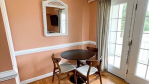 A dining area with a round table, four chairs, a white-framed mirror, and a door with curtains.