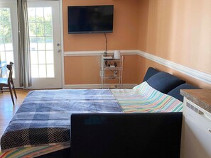 Quarto de hotel com cama, televisão na parede, régua de tomadas e janela com cortinas.