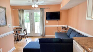 A living room with a sofa, a television mounted on the wall, a dining table with chairs, and a ceiling fan.