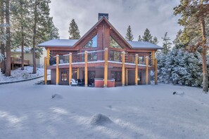 A log cabin with a deck and a covered porch, surrounded by snow-covered trees. - Custom Built Log Cabin, Deschutes River, floating (Sunriver)
