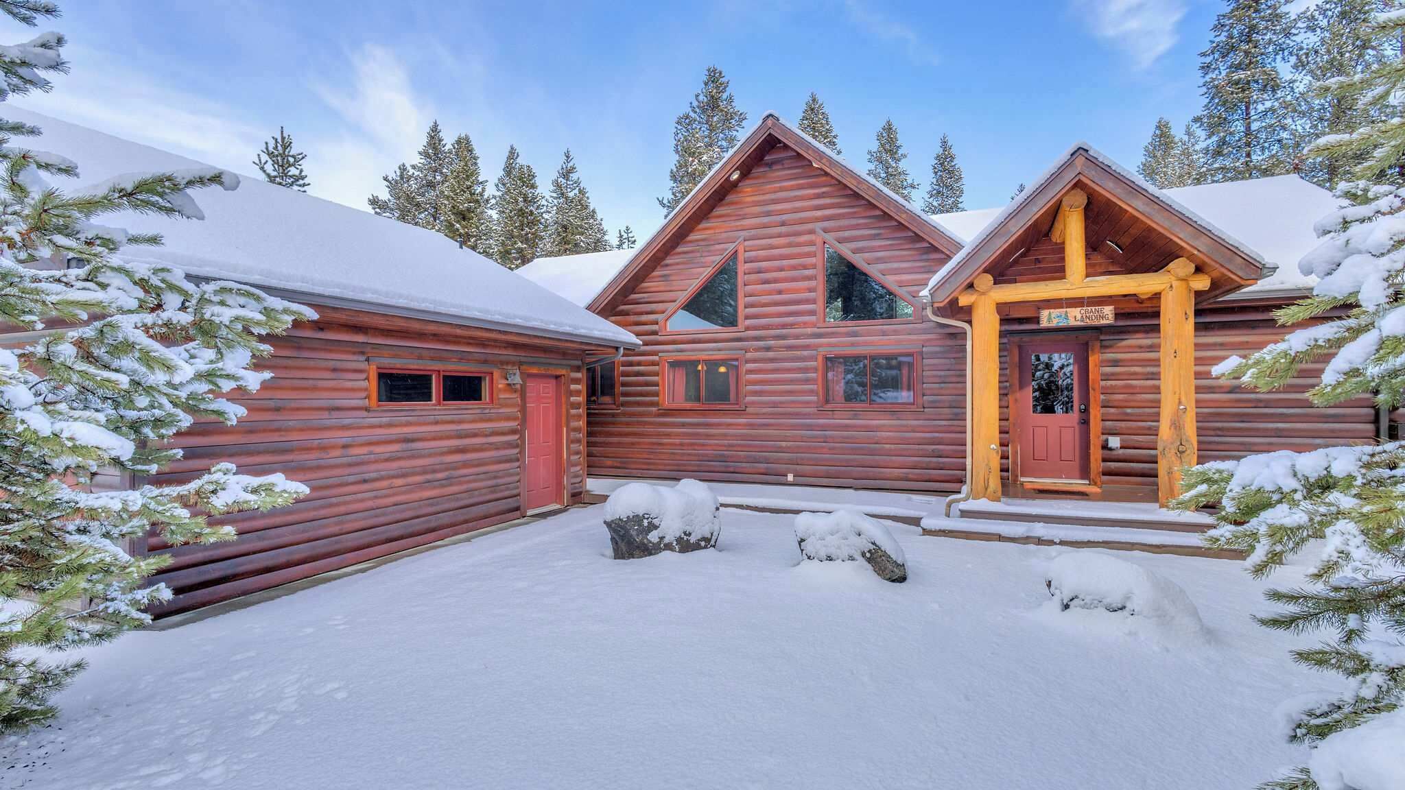 A log cabin with a red door, a covered porch, and a snow-covered landscape.
