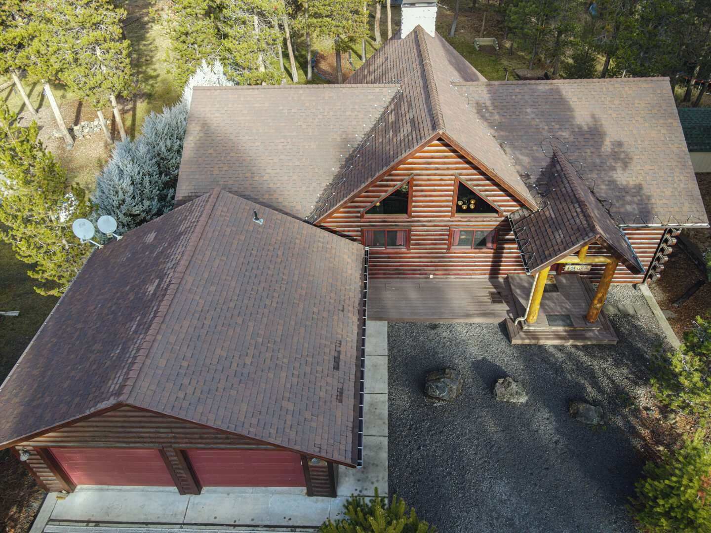 Eine Blockhütte mit einem steilen Satteldach, einer Holzterrasse und einer Schotterauffahrt.