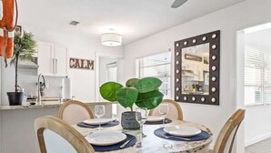 A dining area with a round table, chairs, a plant, and a mirror with lights.