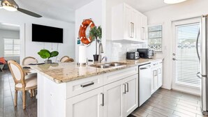 A modern kitchen with white cabinets, a granite countertop, a built-in oven, and a ceiling fan.