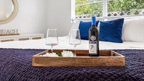 A bedroom with a bed, a window with a view of greenery, and a tray with a bottle and glasses.