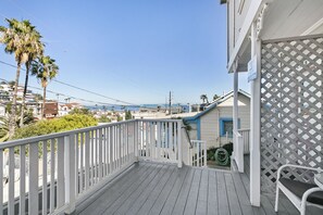 Eine Holzterrasse mit weißer Geländer, mit Blick auf eine Wohngegend mit Häusern und Palmen.