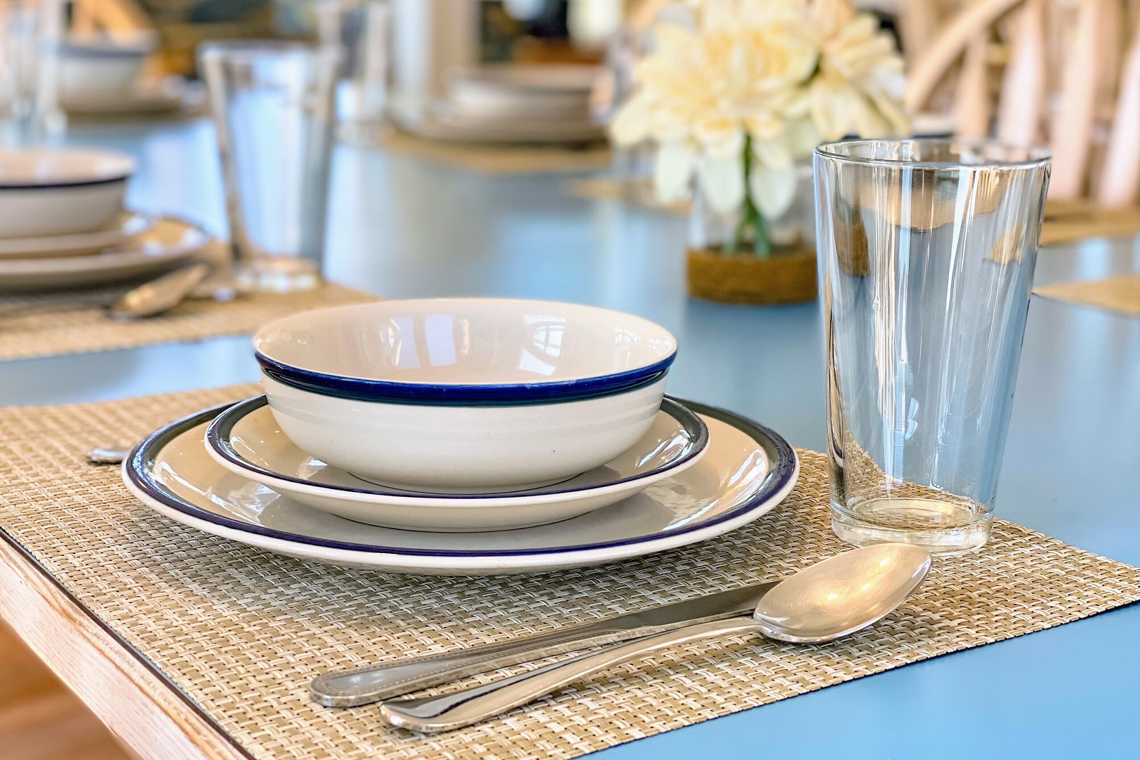 Une table à manger avec un ensemble de vaisselle bleu et blanc, un verre transparent et une cuillère posés sur un set de table en fibres tressées.