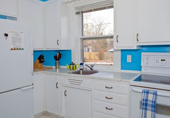 A kitchen with white cabinets, a blue accent wall, a window, a sink, a kettle, and a stove. - Abigail House, 19th Century House (Niagara-on-the-Lake)