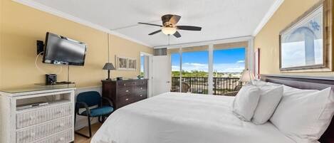 A hotel room with a bed, a desk with a television, a chair, a dresser, and a balcony with a view.