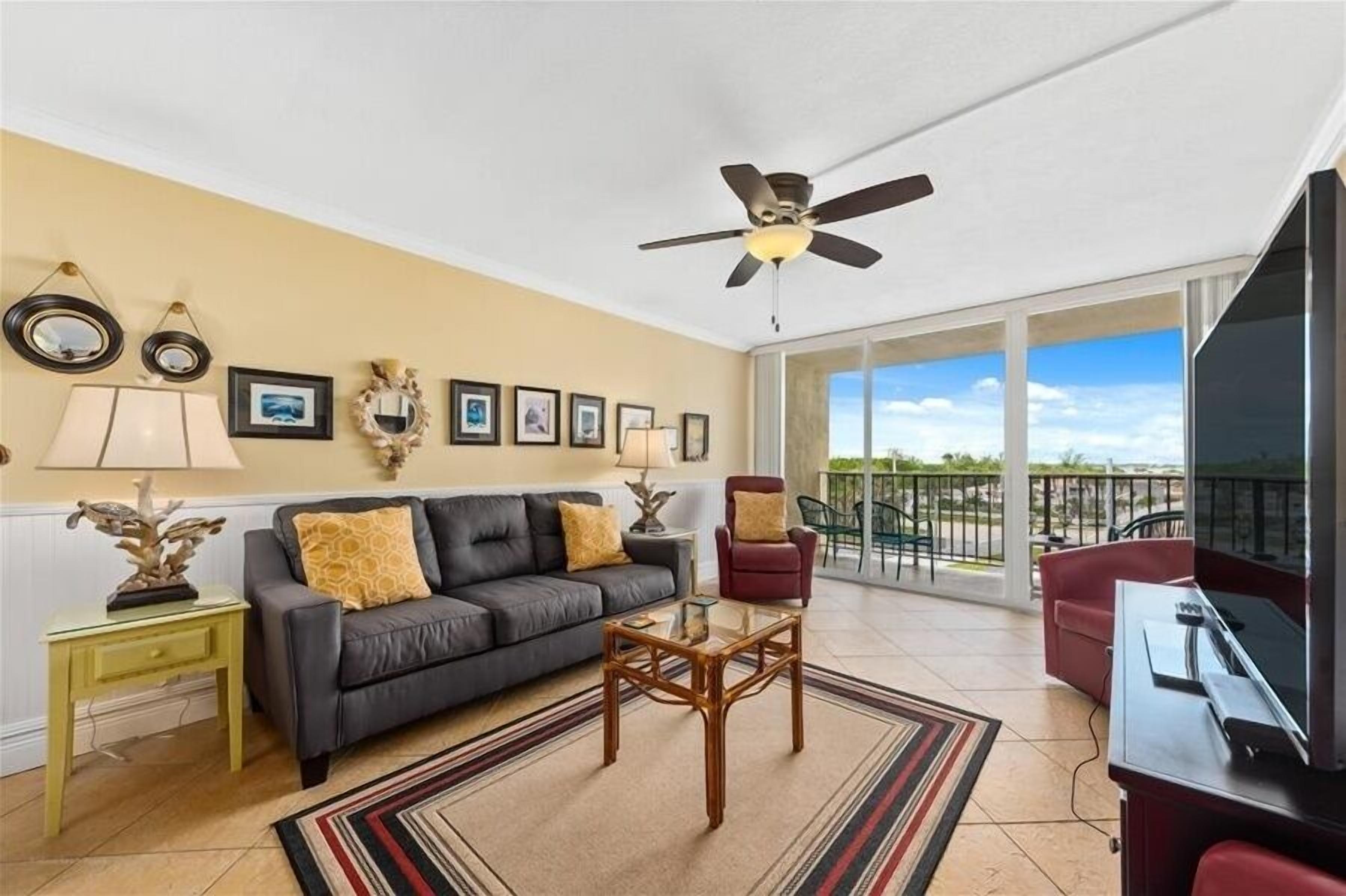 A living room with a sofa, armchairs, a coffee table, a TV, and a balcony with a view.