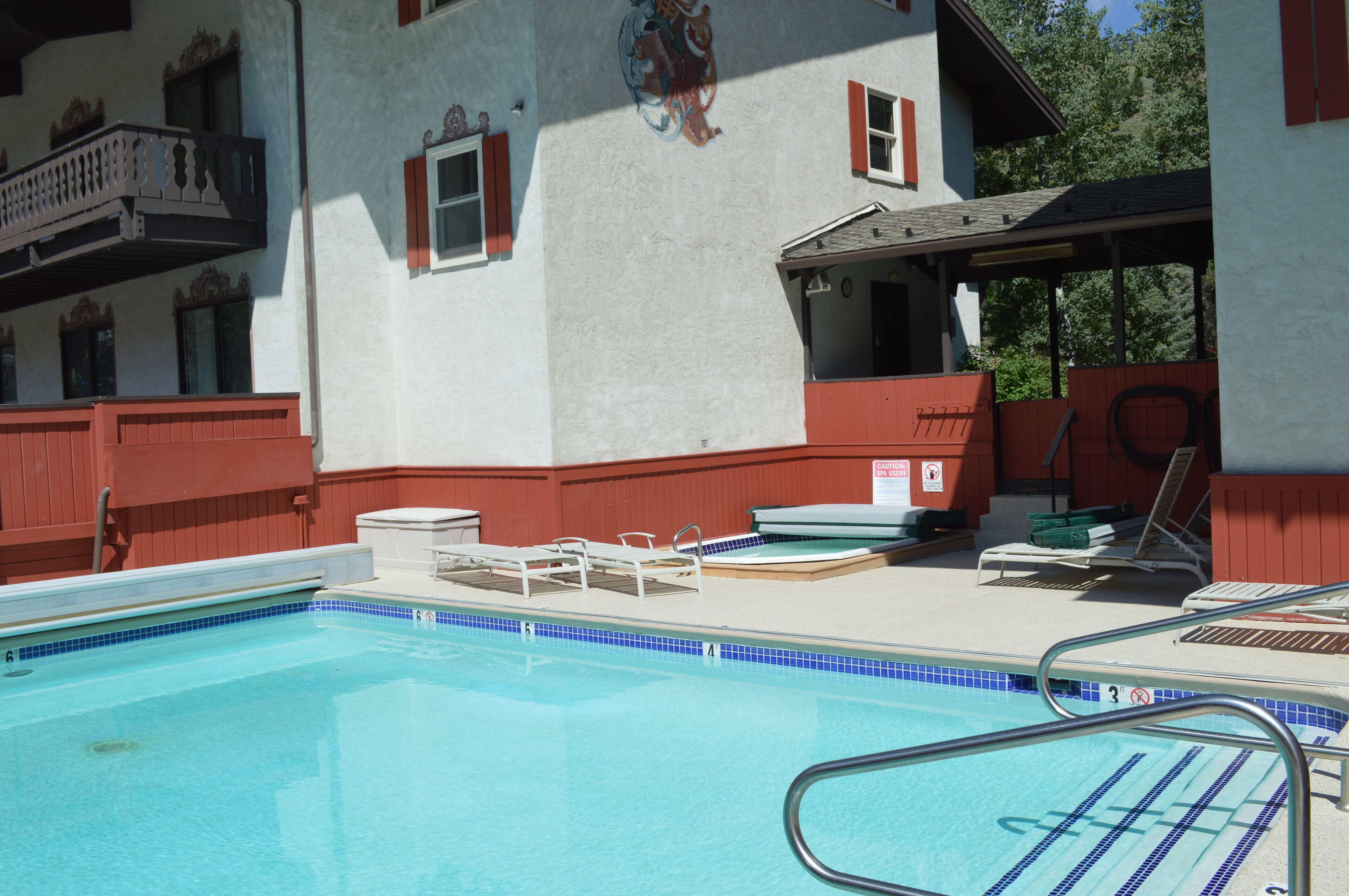 A swimming pool with lounge chairs and a covered area, surrounded by a building with red accents and a mural.