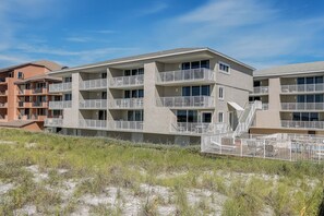 Un hôtel à plusieurs étages doté de balcons, avec une plage de sable au premier plan et un ciel dégagé.