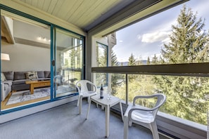 Relax in this spacious living area with a sofa, coffee table, and balcony overlooking a serene forest.