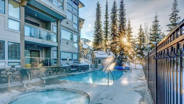 A hotel with a pool, outdoor seating, and a view of snow-covered trees. - Greystone Lodge 311 Ski-in/Out by Acer Vacations (Whistler)