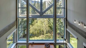 A room with a large window, a fireplace, and a view of a forest. - Greystone Lodge 311 Ski-in/Out by Acer Vacations (Whistler)