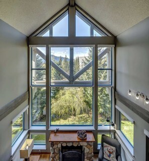 A room with a large window, a fireplace, and a view of a forest. - Greystone Lodge 311 Ski-in/Out by Acer Vacations (Whistler)