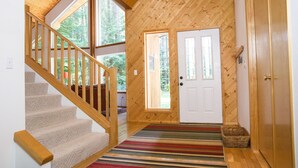 Un interior de madera con una escalera, una puerta y vistas al exterior.