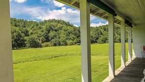 Eine überdachte Veranda mit Blick auf ein grünes Feld und einen bewaldeten Hügel.