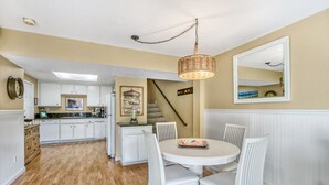 A kitchen with white cabinets, a dining table with white chairs, and a hanging light fixture.