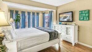A bedroom with a bed, a TV, a dresser, and a window with curtains.