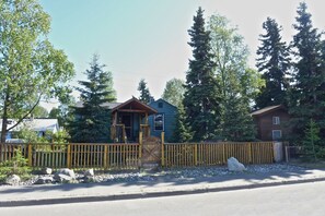 Una baita con veranda in legno, circondata da alberi e da una recinzione.