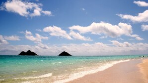 Une plage à l’eau turquoise et limpide, un rivage sablonneux et, au loin, deux formations terrestres sombres.