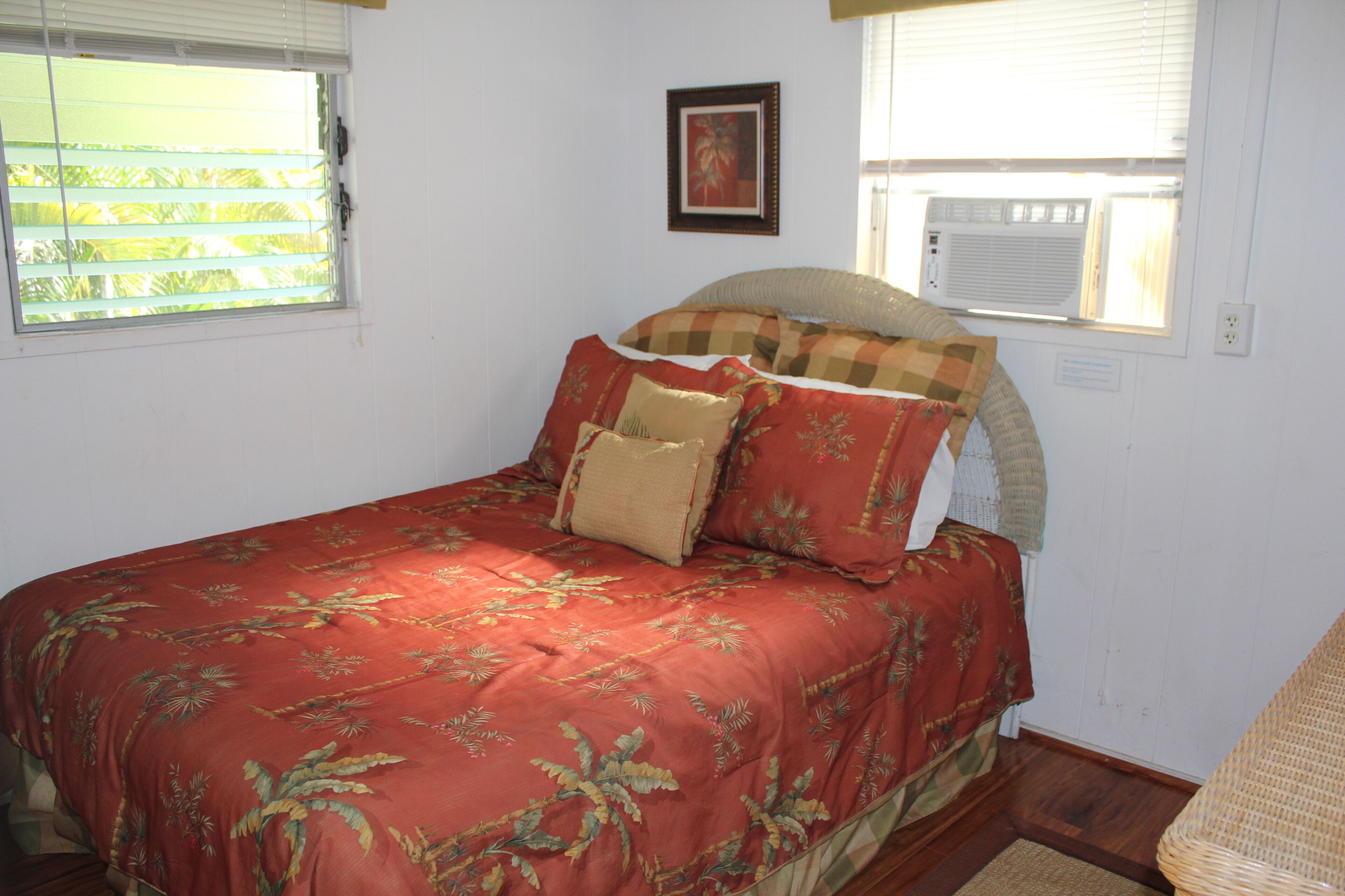 A bedroom with a bed, a window with blinds, a wall-mounted air conditioner, and a framed picture.