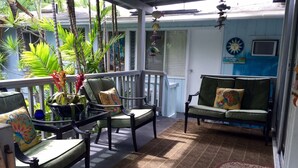 Un espace extérieur aménagé, abrité et doté de chaises et d’un canapé, entouré de plantes tropicales et agrémenté d’un mur décoratif.