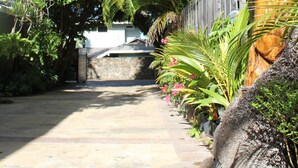 Un chemin de pierres qui traverse un jardin tropical, avec une sculpture en bois et différentes plantes.