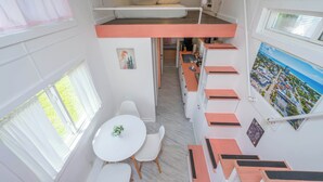 A compact room with a bunk bed, a small kitchenette, a dining area with a table and chairs, and a view of the outdoors through a window.