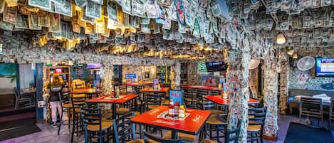 A restaurant interior with tables and chairs, surrounded by walls covered in currency notes.