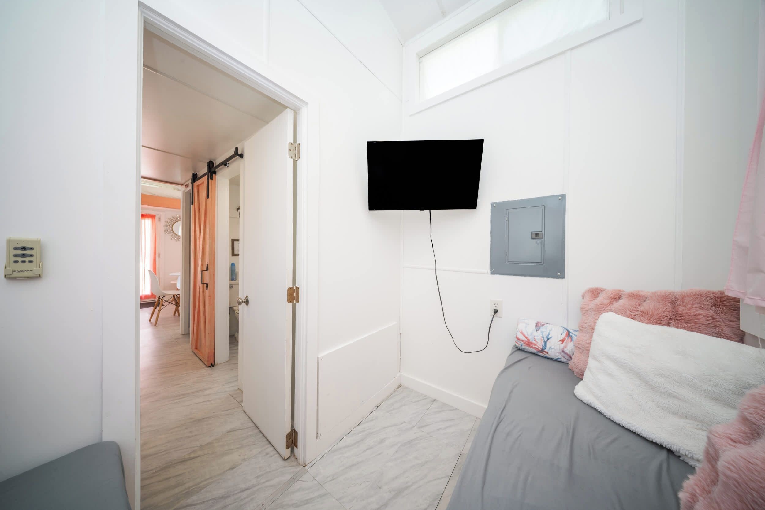 A bedroom with a bed, a TV mounted on the wall, and a door leading to another room.