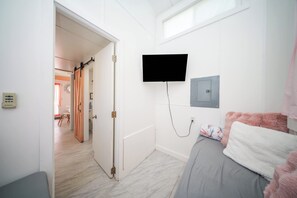 Un dormitorio con una cama, un televisor montado en la pared y una puerta que da a otra habitación.