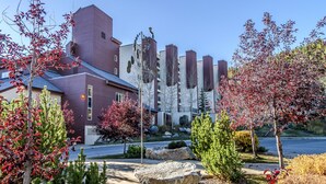 Un edificio moderno con paredes exteriores en tonos rojo y blanco, rodeado de jardines ajardinados con varios árboles y una gran formación rocosa.