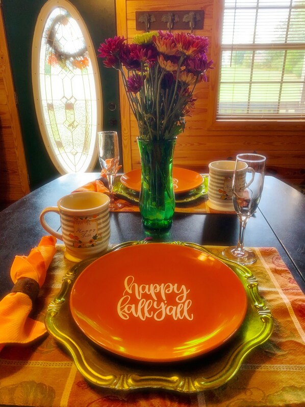 A dining table with a green vase of flowers, a plate with "happy fall" written on it, and a glass.