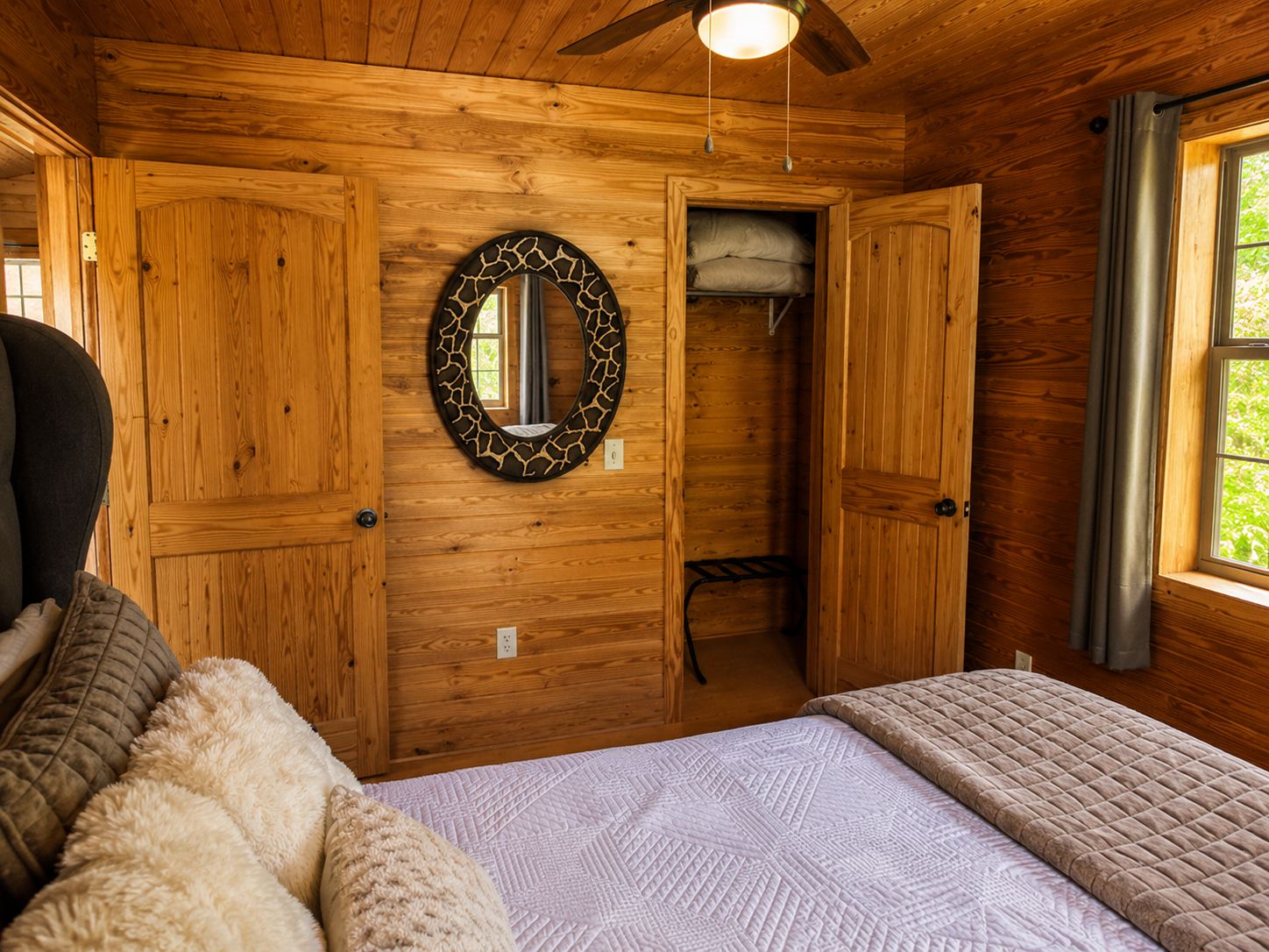 A wooden cabin room with a bed, a mirror, and a window.