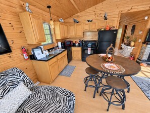 A compact kitchen with wooden cabinets, a dining table with stools, and a fireplace.