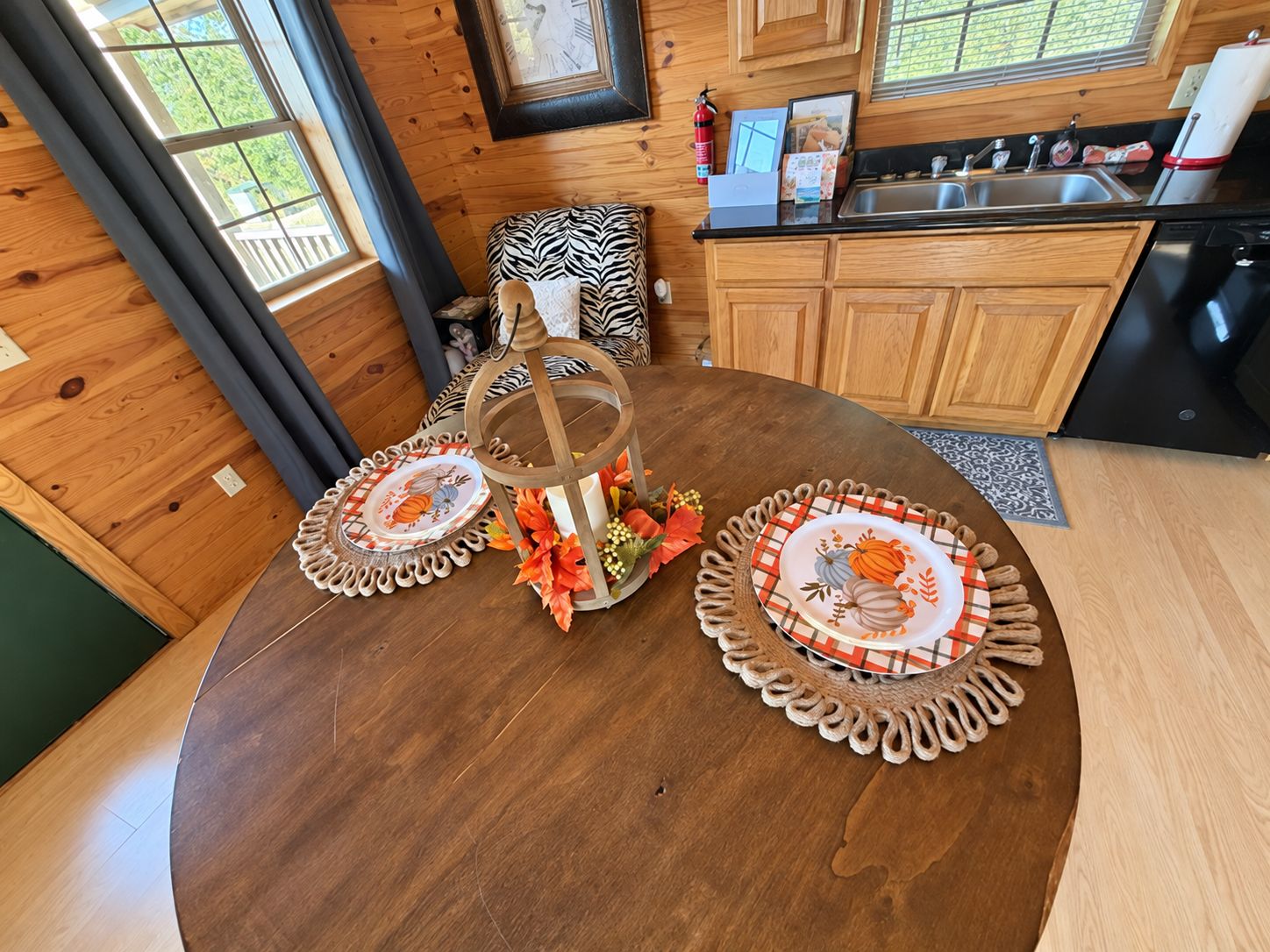 Een houten eettafel met een kaarsenhouder in het midden, omringd door placemats met herfstmotieven.