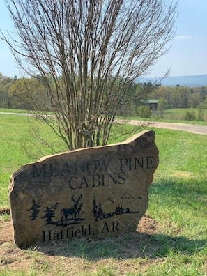 A stone sign for Meadow Pine Cabins in Hatfield, AR, with a depiction of a cabin, trees, and mountains.