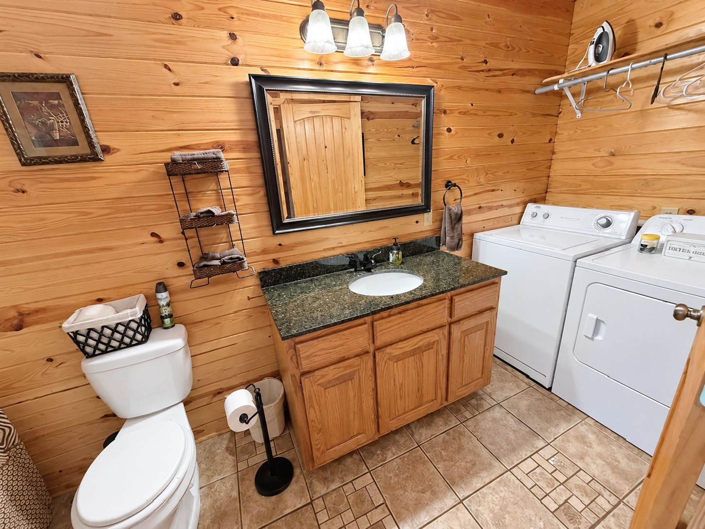 A compact bathroom with a wooden vanity, a sink, a toilet, and a washing machine.