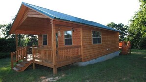 A wooden cabin with a porch, a covered deck, and a small staircase leading to the entrance.