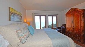 A bedroom with a large bed, a wooden wardrobe, and a view of the sea through the windows. - H319: 1BD Villa w/ Spectacular Views,Fireplace,Romantic Private Balcony,NEW Cart (Avalon)