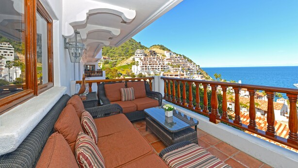A balcony with wicker furniture, a glass coffee table, and a view of the sea and buildings. - H319: 1BD Villa w/ Spectacular Views,Fireplace,Romantic Private Balcony,NEW Cart (Avalon)