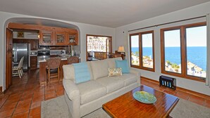 A living room with a sofa, coffee table, and a view of the ocean through large windows. - H319: 1BD Villa w/ Spectacular Views,Fireplace,Romantic Private Balcony,NEW Cart (Avalon)