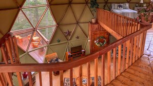 A geodesic dome structure with a wooden staircase, a small seating area, and a view of the outdoors. - Unique Handcrafted Geodesic Dome w/2 Fire Pits & Hot Tub – 40+ Private Acres (Grassy Creek)