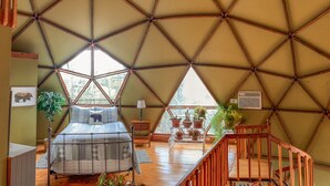 A geodesic dome room with a bed, a small table, and a staircase. - Unique Handcrafted Geodesic Dome w/2 Fire Pits & Hot Tub – 40+ Private Acres (Grassy Creek)