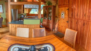 A rustic cabin interior with a wooden dining table, chairs, a kitchen area with a sink and cabinets, and a large wooden door with a welcome sign. - Unique Handcrafted Geodesic Dome w/2 Fire Pits & Hot Tub – 40+ Private Acres (Grassy Creek)